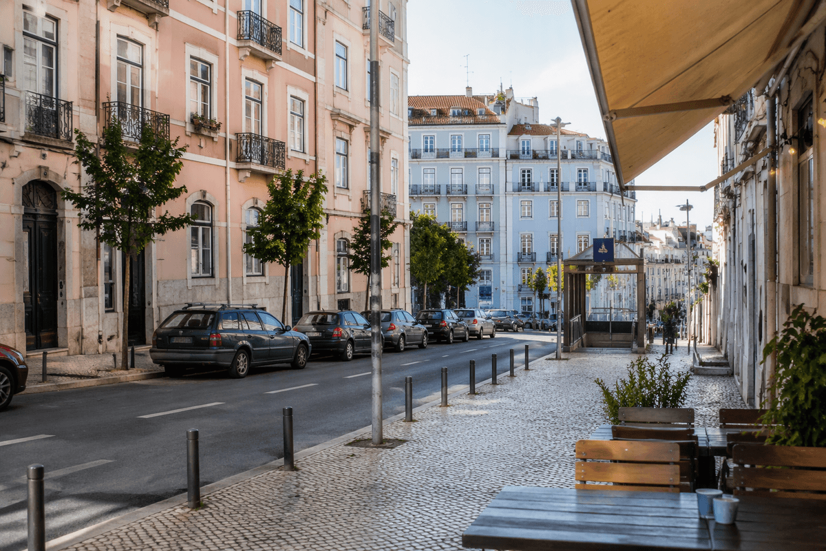 A calm Lisbon neighborhood street with apartment buildings, a cafe, and nearby public transit.